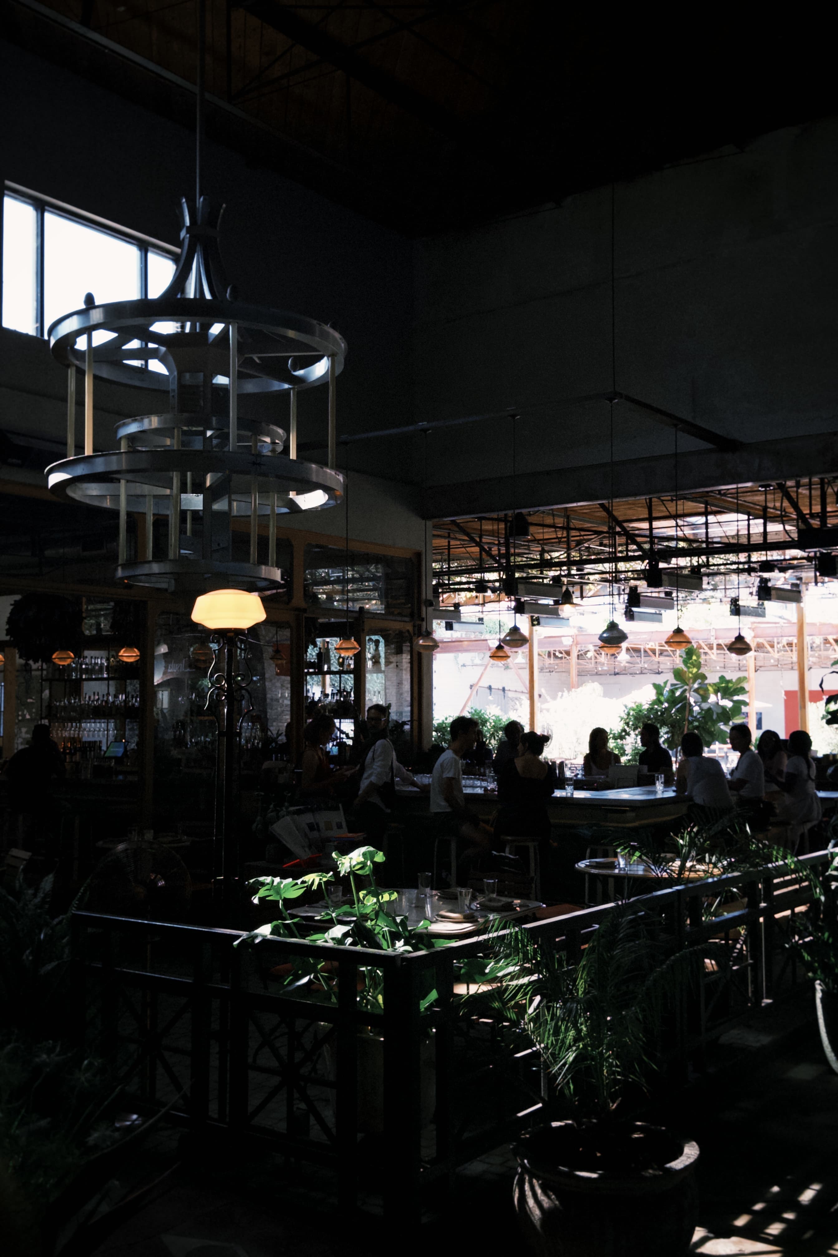 A dim restaurant interior with a sculptural hanging light and a busy bar